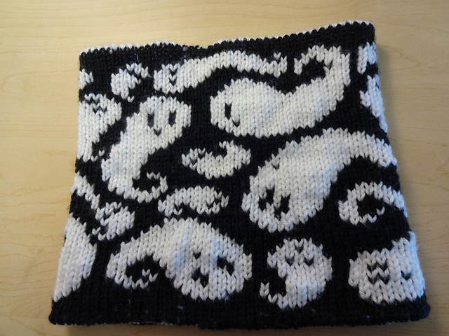 A handknit cowl showing many whimsical white ghosts on a black background.