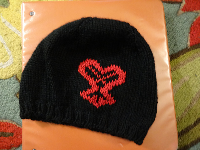A black handknit hat with the Heartless symbol from Kingdom Hearts in red. The symbol is shaped like a fleur de lis with a heart instead of the top half and two lines crossing through it.
