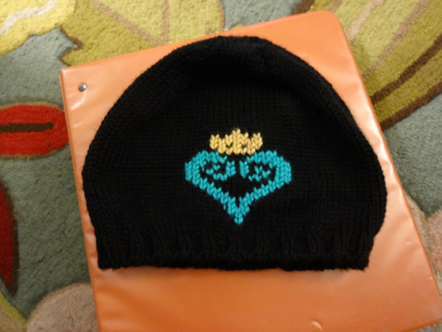 A black handknit hat with the Kingdom Hearts logo on it. The logo is a teal stylized heart with a Disney crown on top.
